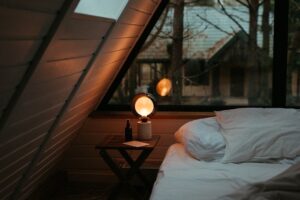 Gemütliches Zimmer mit warm leuchtender Lampe neben einem weißen Bett