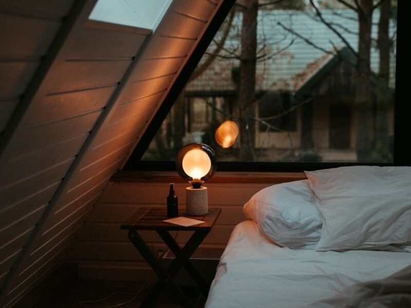 Gemütliches Zimmer mit warm leuchtender Lampe neben einem weißen Bett
