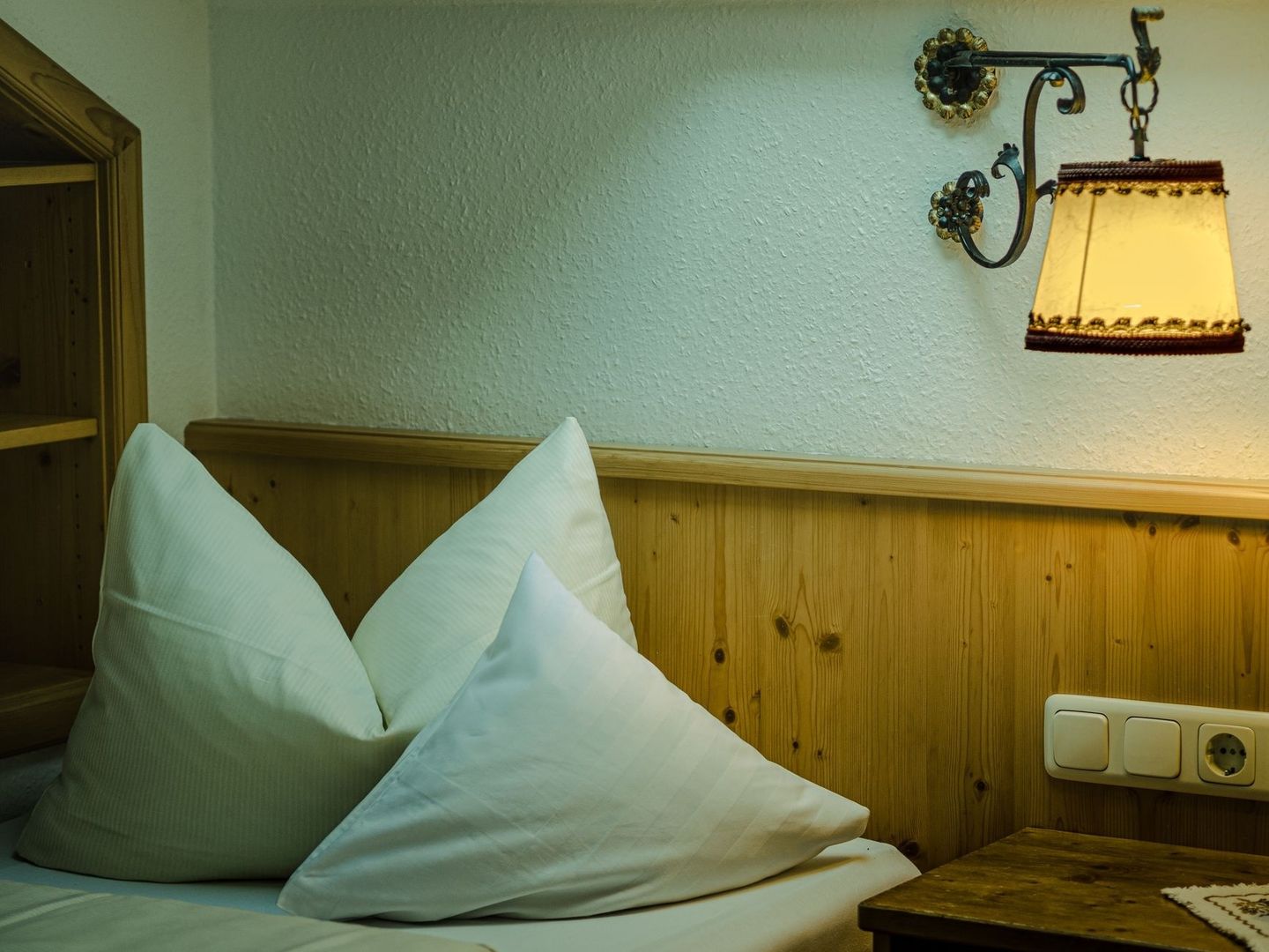 Warm leuchtende Wandleuchte neben einem Hotelbett mit weißen Kissen