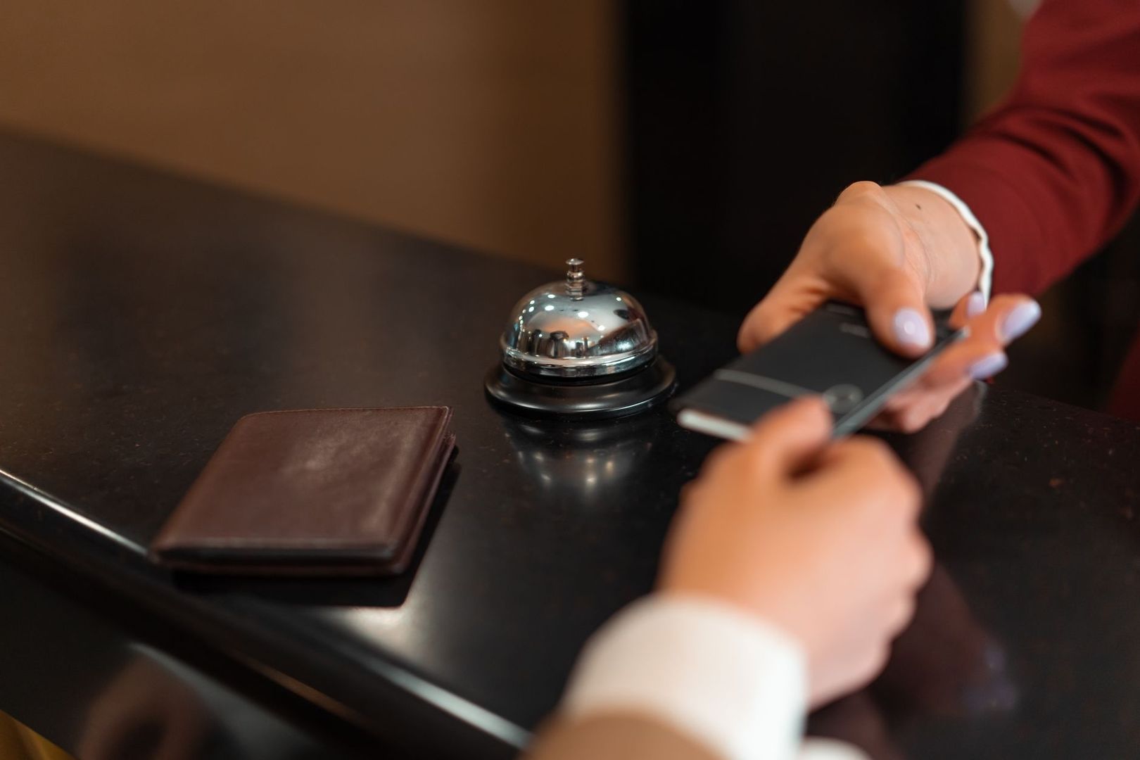 Smartphone neben Hotelglocke und Lederetui auf einem Empfangstresen